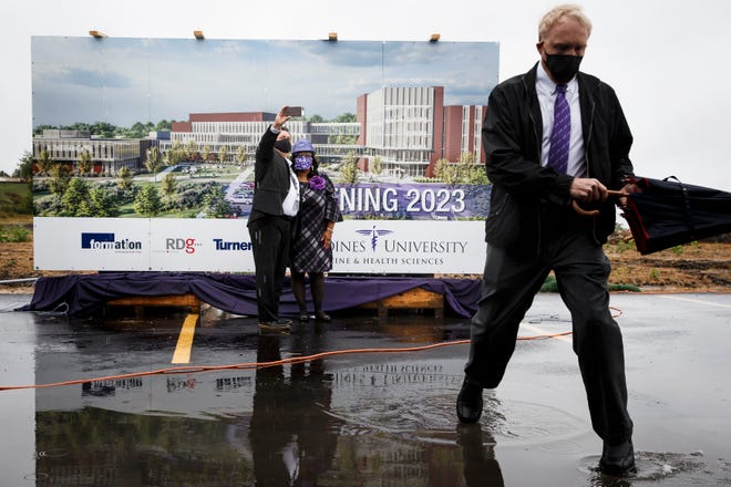 Trustee Renee Hardman, right, and Chief Diversity Officer Dr. Rich Salas, left, take a selfie in front of renderings of DMU's new campus as Trustee Dr. Michael Witte avoids puddles during a groundbreaking ceremony on Thursday, Sept. 10, 2020, in West Des Moines.